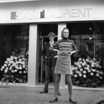 Yves St. Laurent standing outside his Rive Gauche boutique in France, with a model wearing an ensemble from his 1966 collection with “Belle Vivier” pumps.